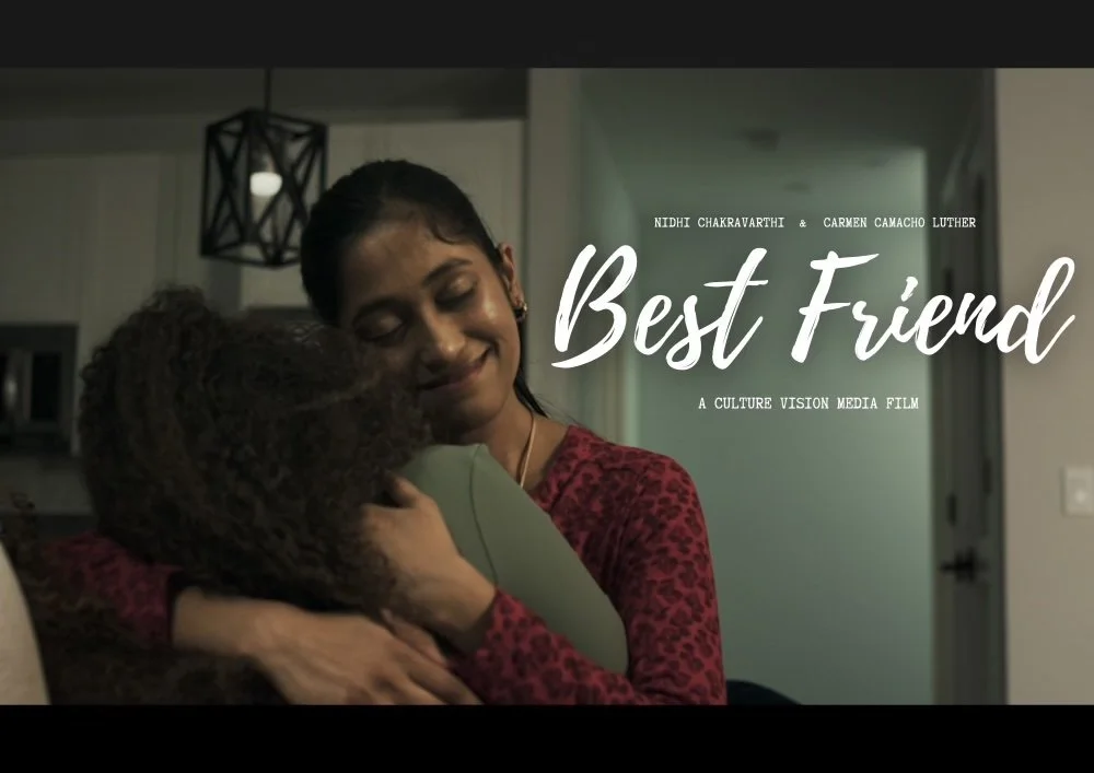 Two women hugging, one with eyes closed and smiling, in a cozy indoor setting with modern decor, promoting the film 'Best Friend' by Nidhi Chakravarthi and Carmen Camacho Luther.