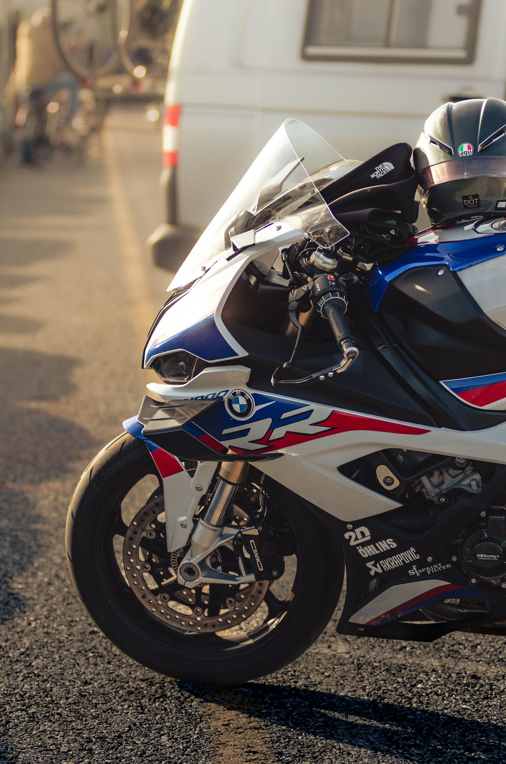 Close-up of a BMW S 1000 RR motorcycle with a blue, white, and red color scheme parked on an asphalt road, with a black helmet and gloves resting on the seat.