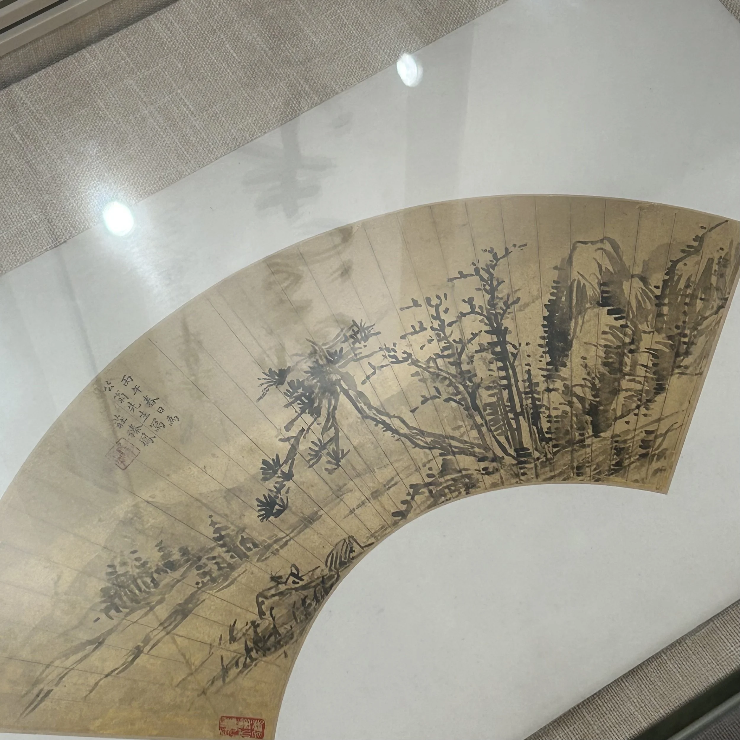 Traditional Chinese ink painting on a fan depicting trees, mountains, and Chinese characters.