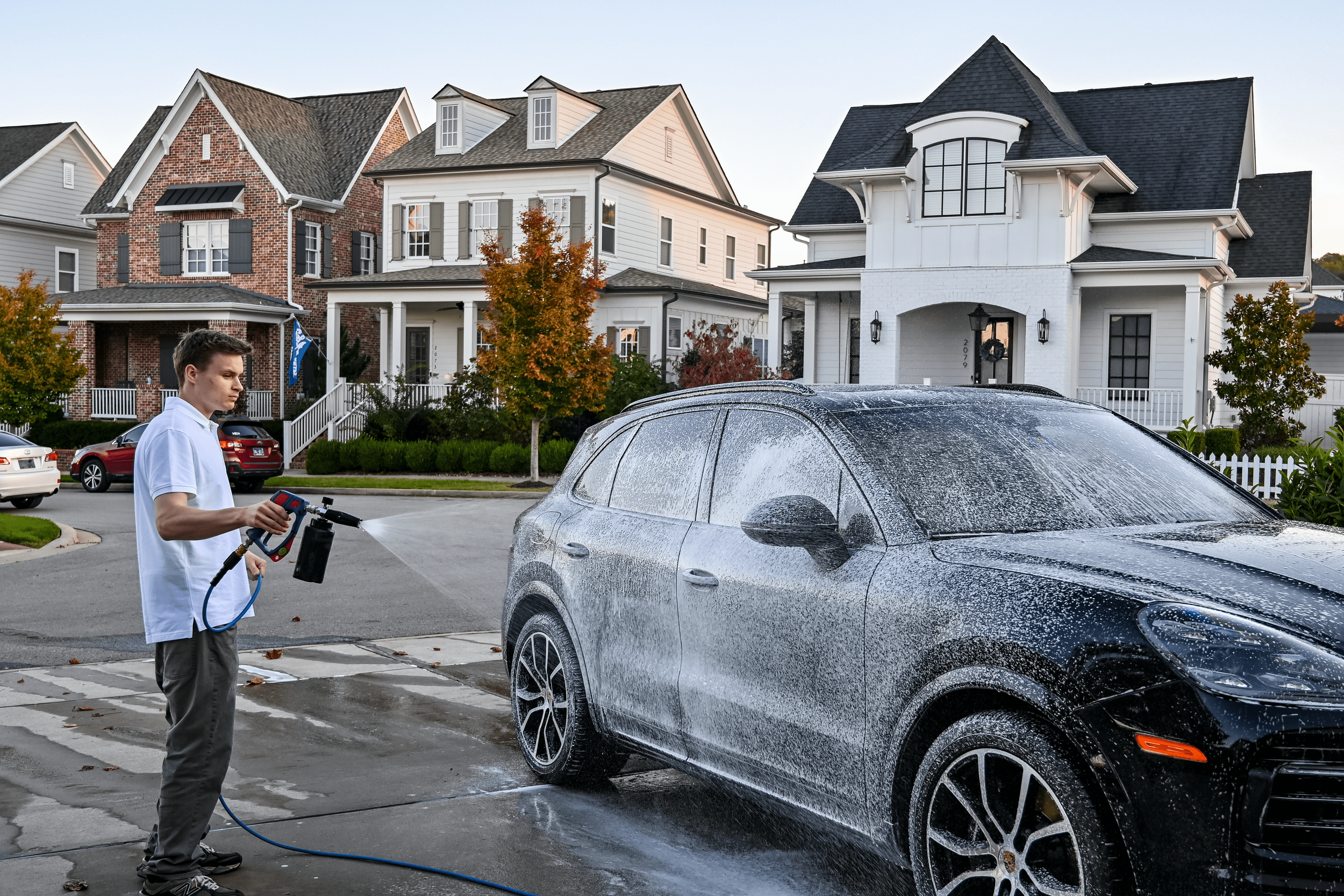 A silver sports car being washed, covered with white foam and soap suds, on a driveway.