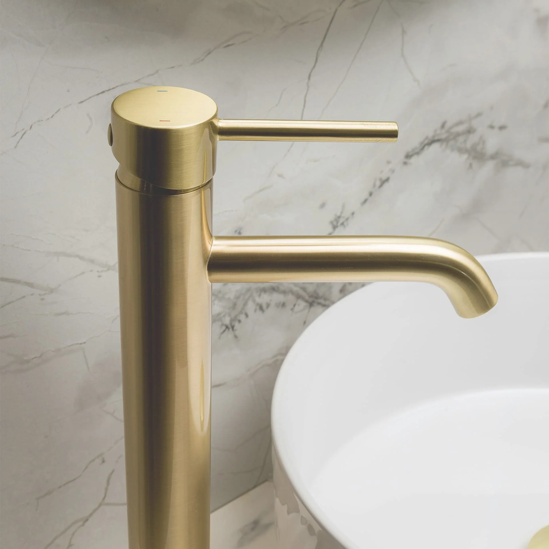 A gold-colored faucet next to a white sink, mounted on a marble wall.