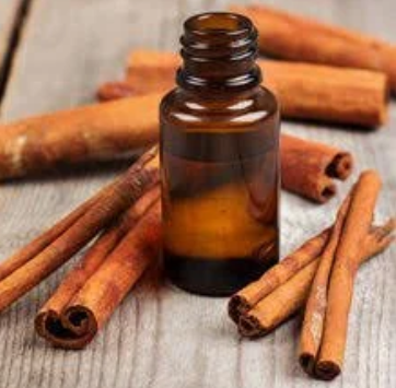 A small amber glass bottle surrounded by cinnamon sticks on a wooden surface.