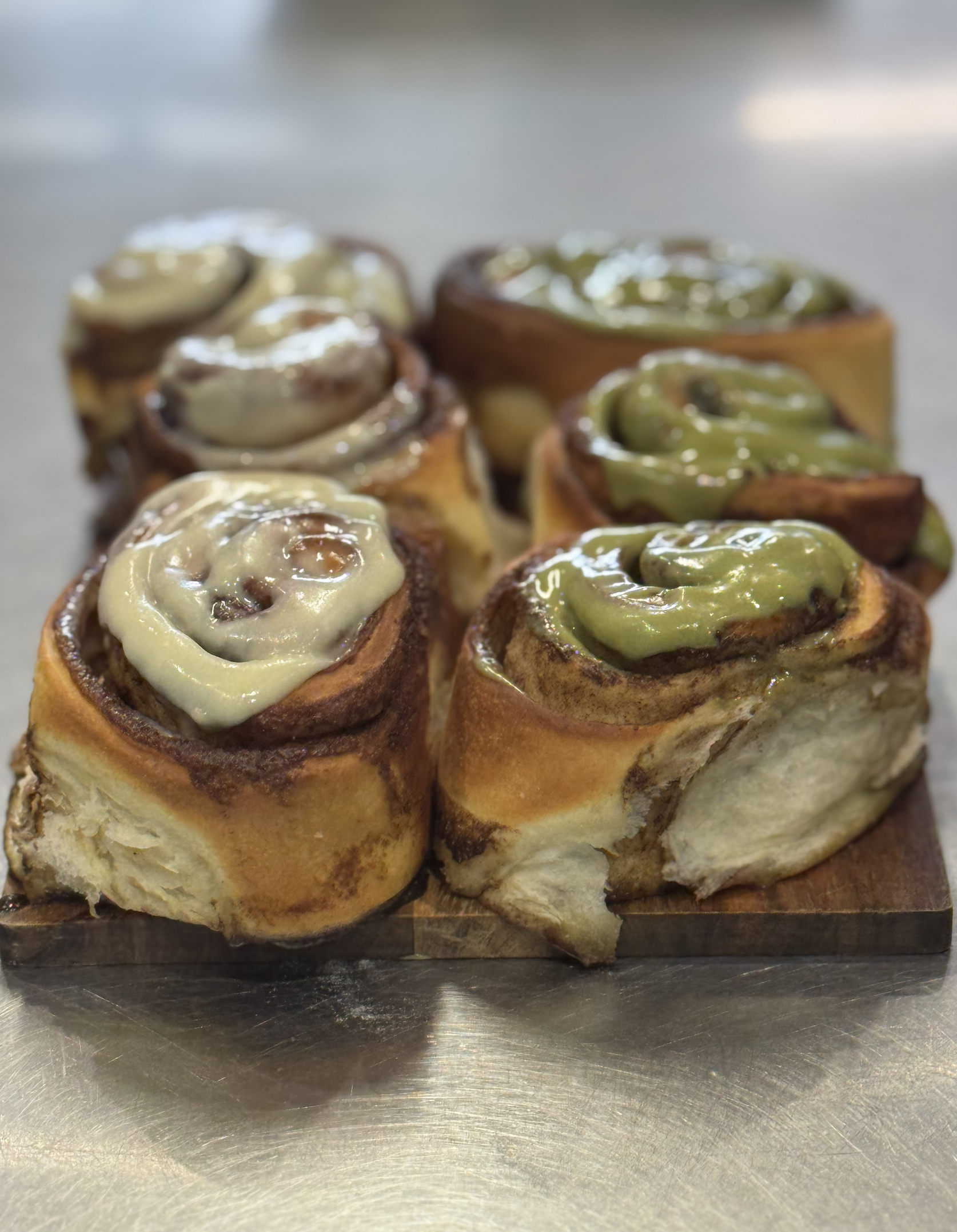 Close-up of cinnamon rolls with green icing on a stainless steel surface.