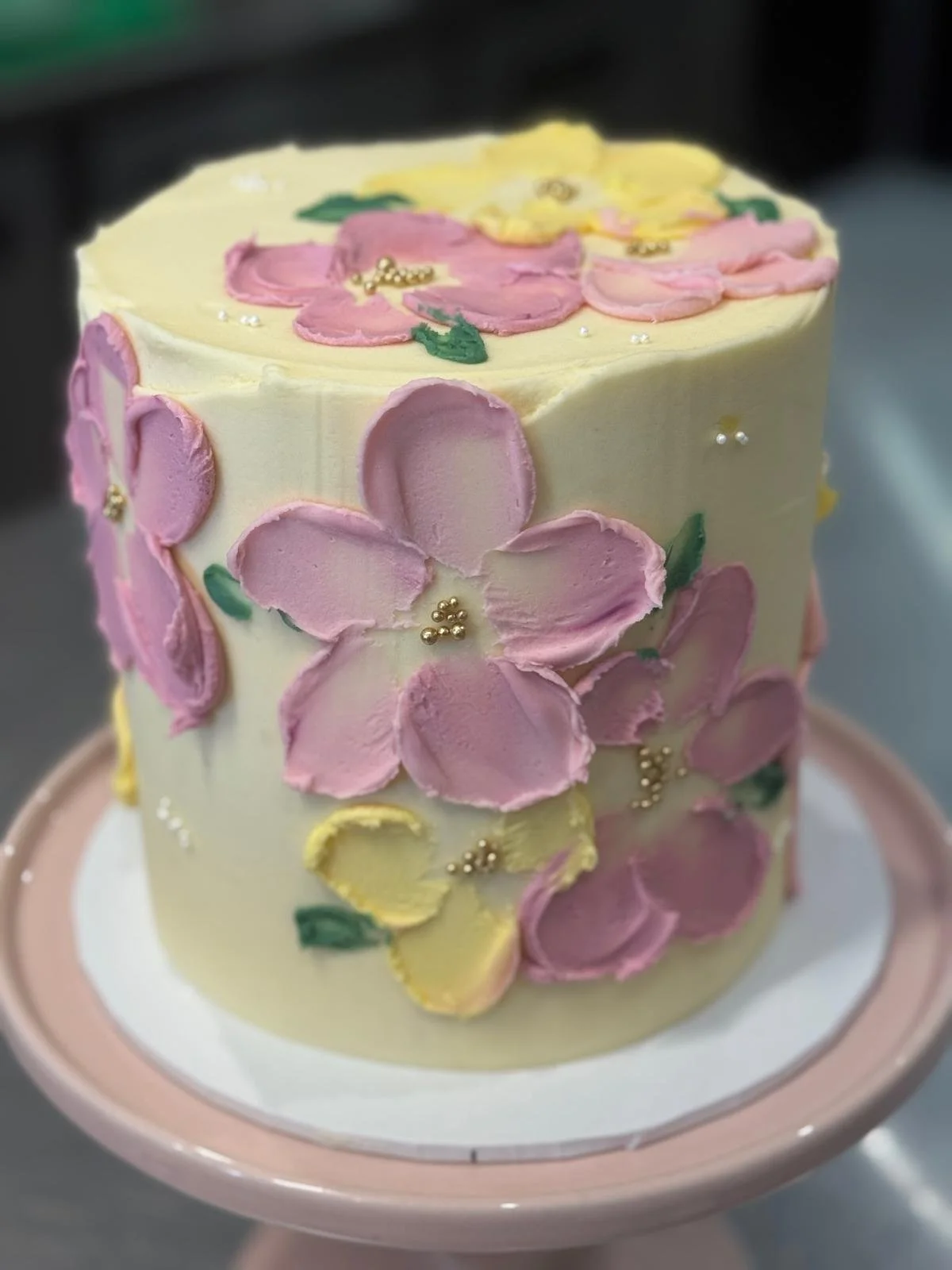 A decorated birthday cake with pink, yellow, and purple flower designs and small edible pearl accents.