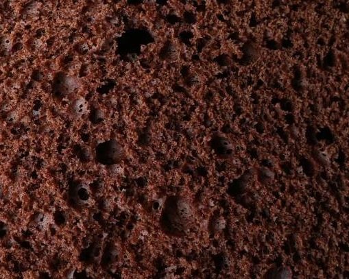 Close-up of chocolate cake's crumb with holes and moist texture.