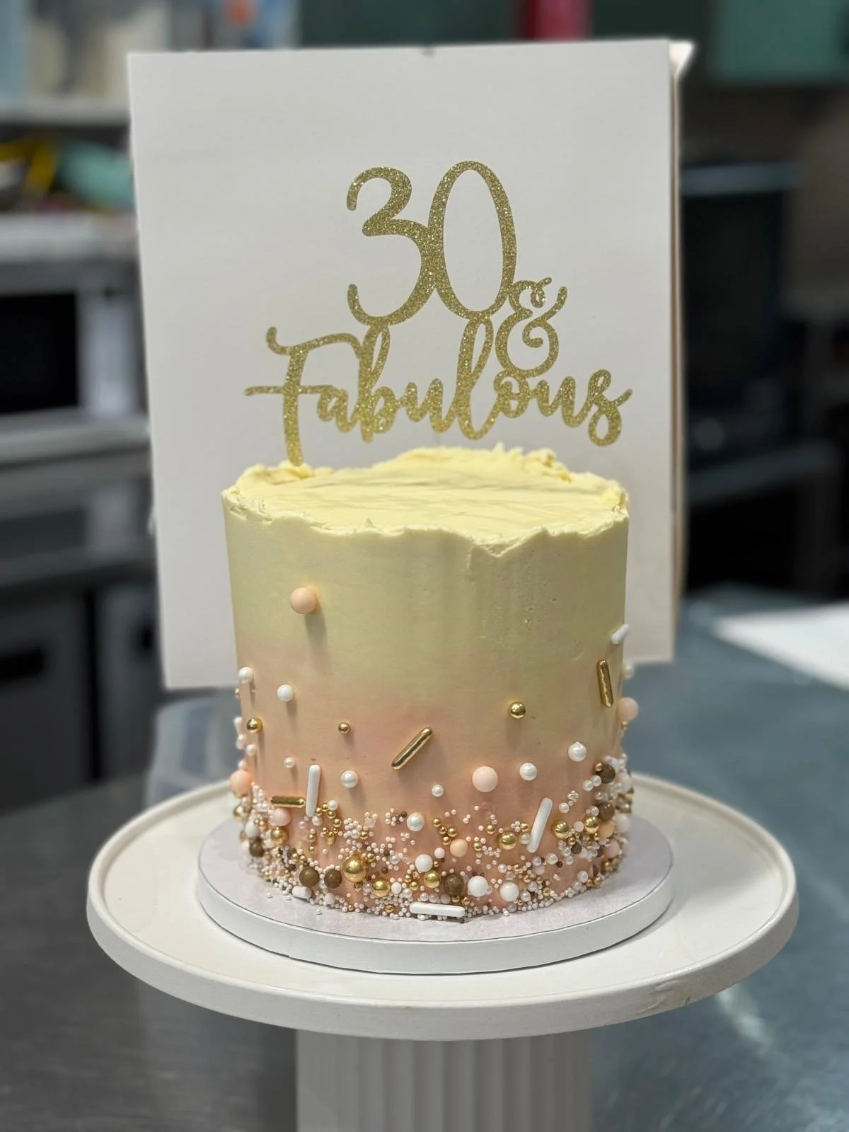 A celebration cake with white, pink, and gold decorations, featuring a topper that says "30 & Fabulous."