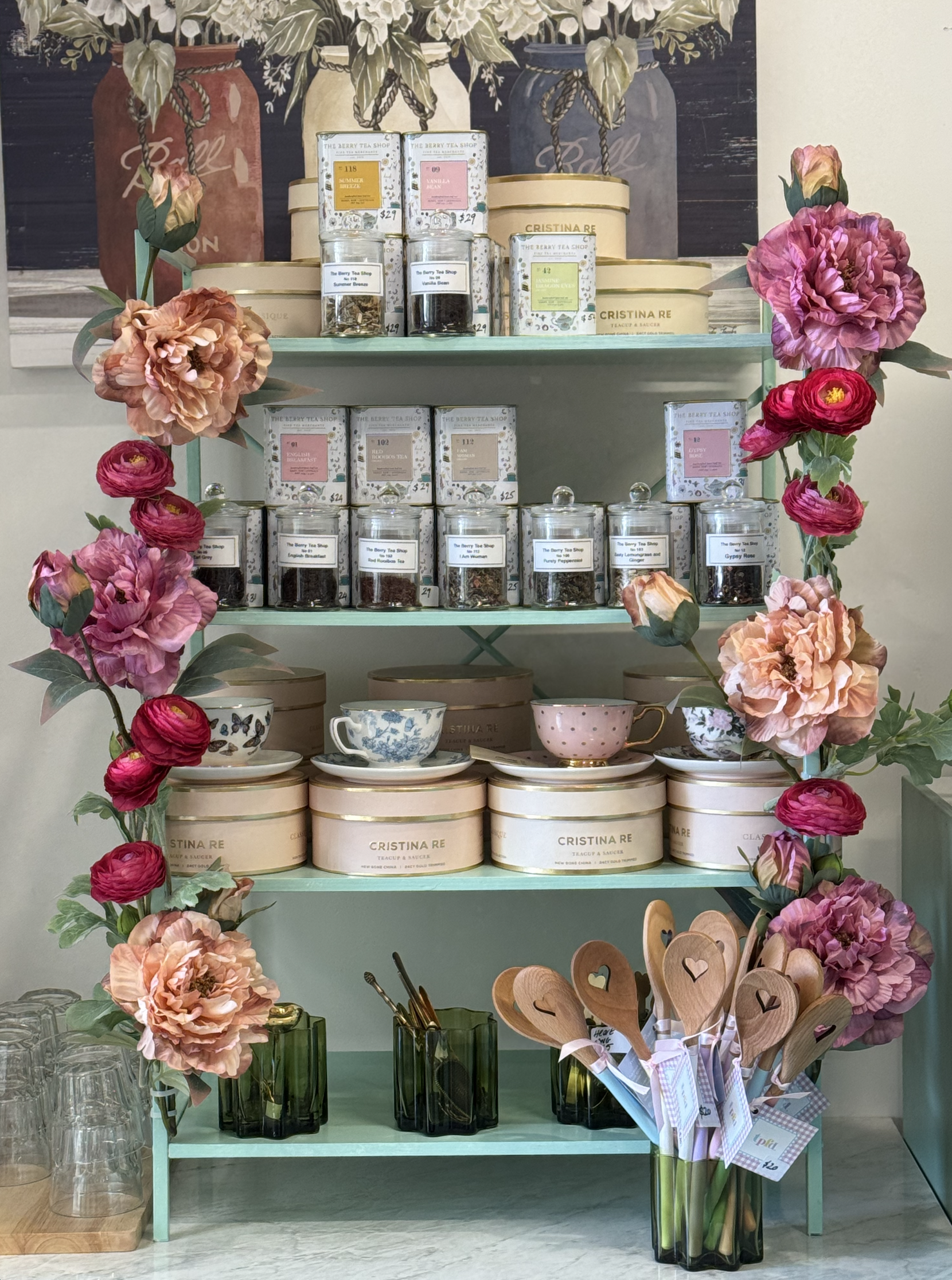 A retail display of teaware products, including teacups and teapots, with flowers and decorative items arranged around it.