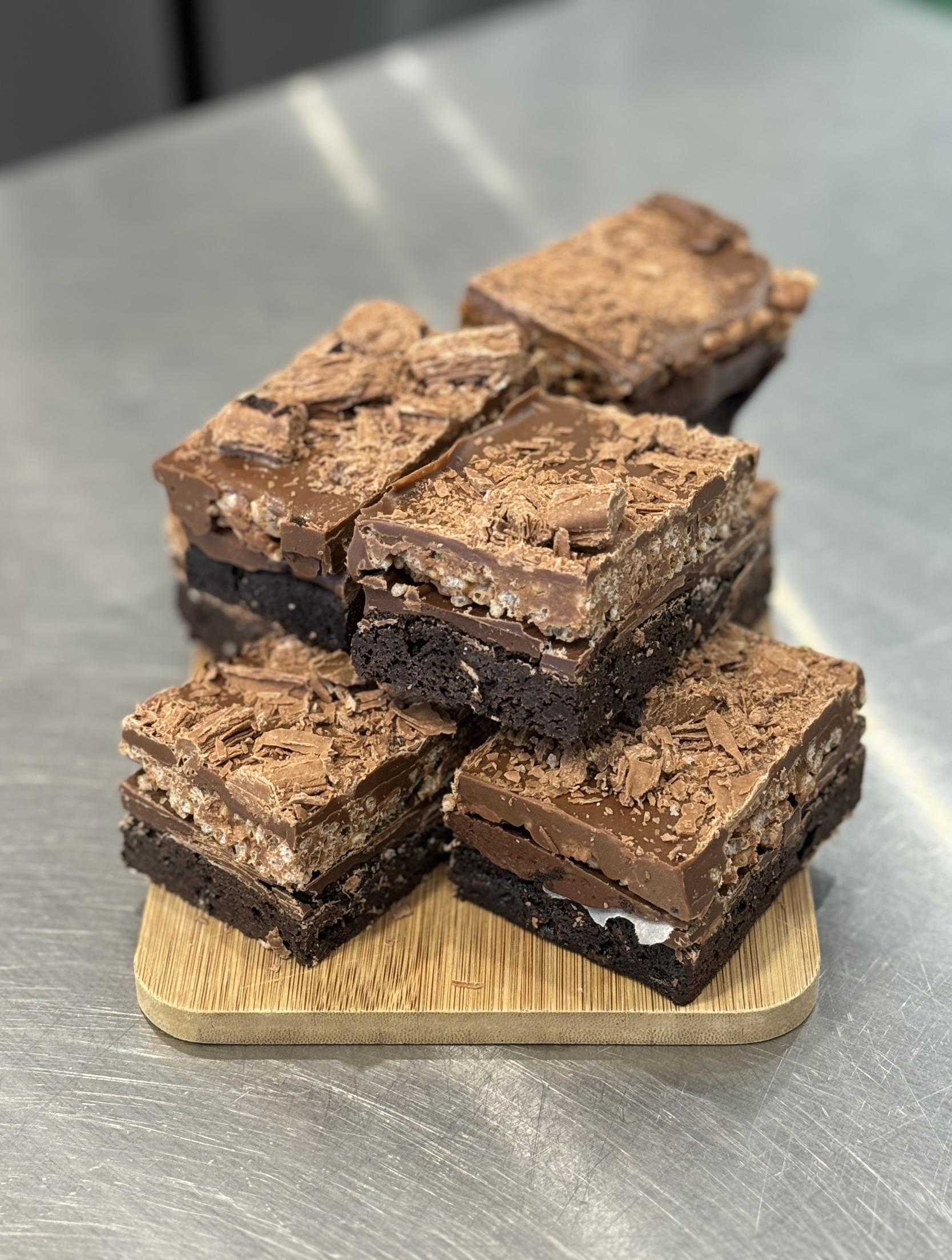 Stack of four assorted chocolate brownies on a wooden cutting board, on a metal countertop.