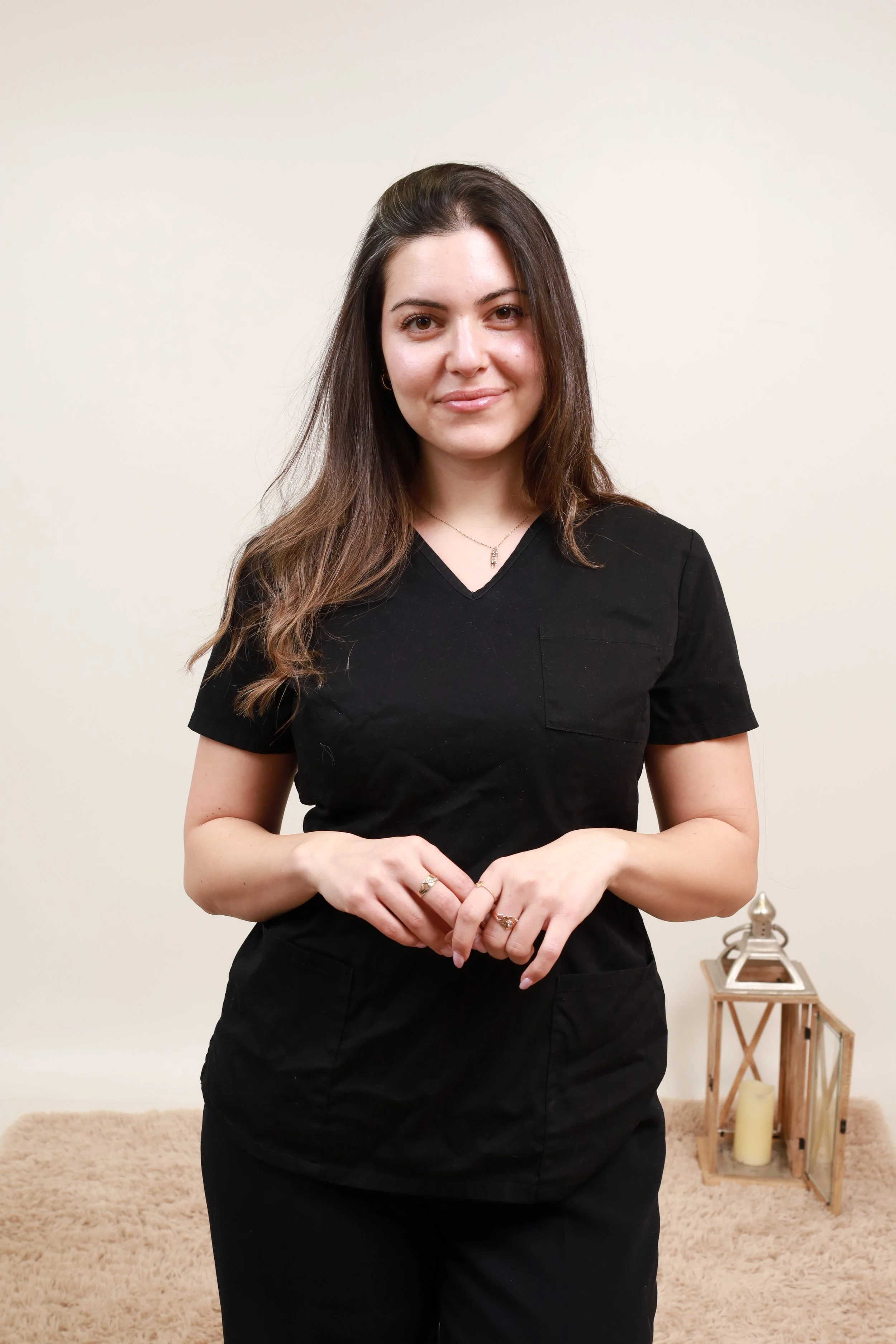 A young woman with long brown hair wearing a black uniform, standing indoors with beige carpet and decorative candle lanterns in the background.
