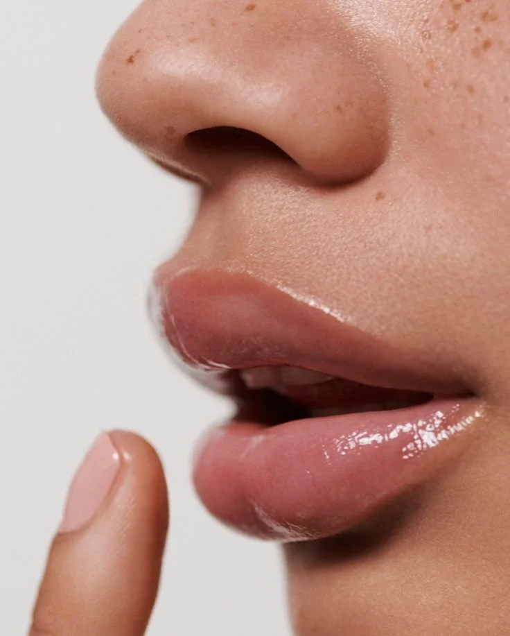 Close-up of a person with glossy lips touching their finger to lips.