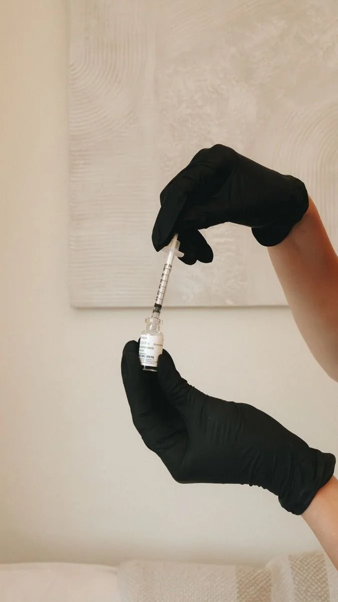 Person wearing black gloves holding a syringe with a vial inside.