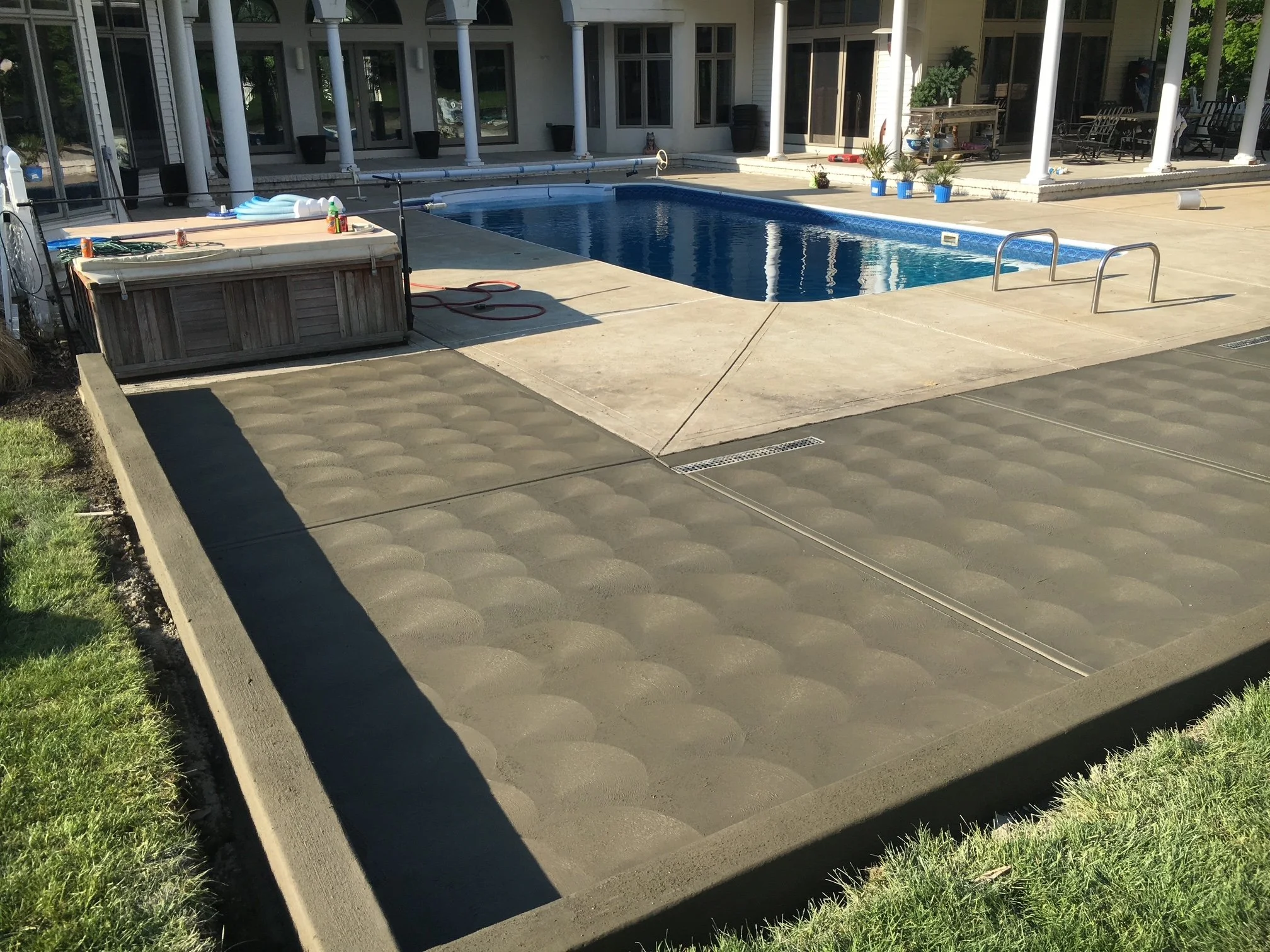 Backyard pool with a wooden hot tub on a concrete patio, surrounded by a lounge area and potted plants.