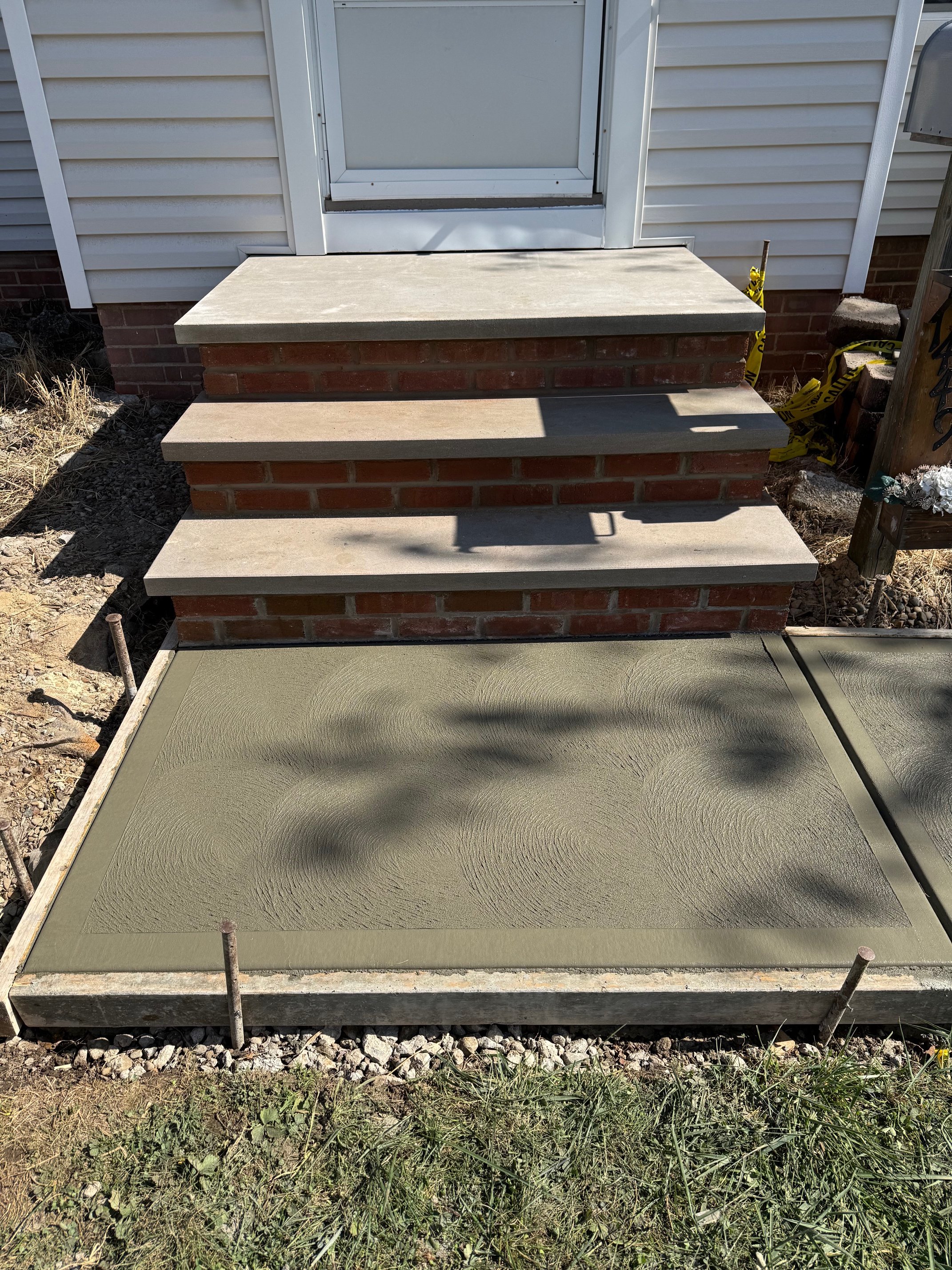 Steps leading to a door with a brick base and concrete treads, and a freshly poured concrete slab in front of the steps.