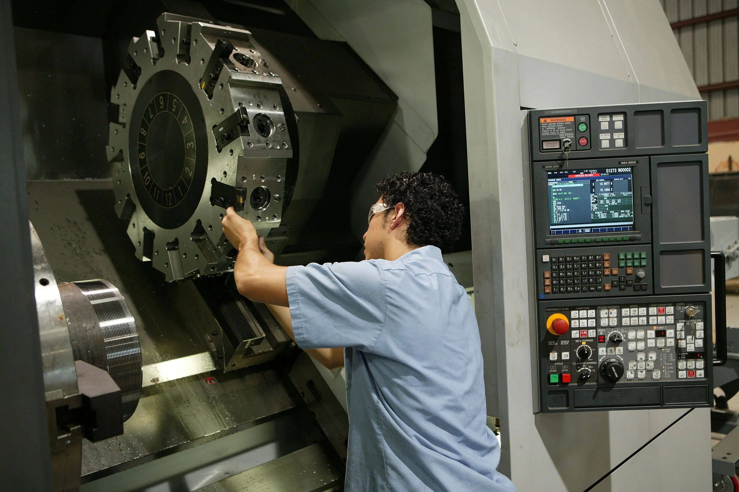 A technician wearing safety goggles working on a large CNC machine in an industrial setting.