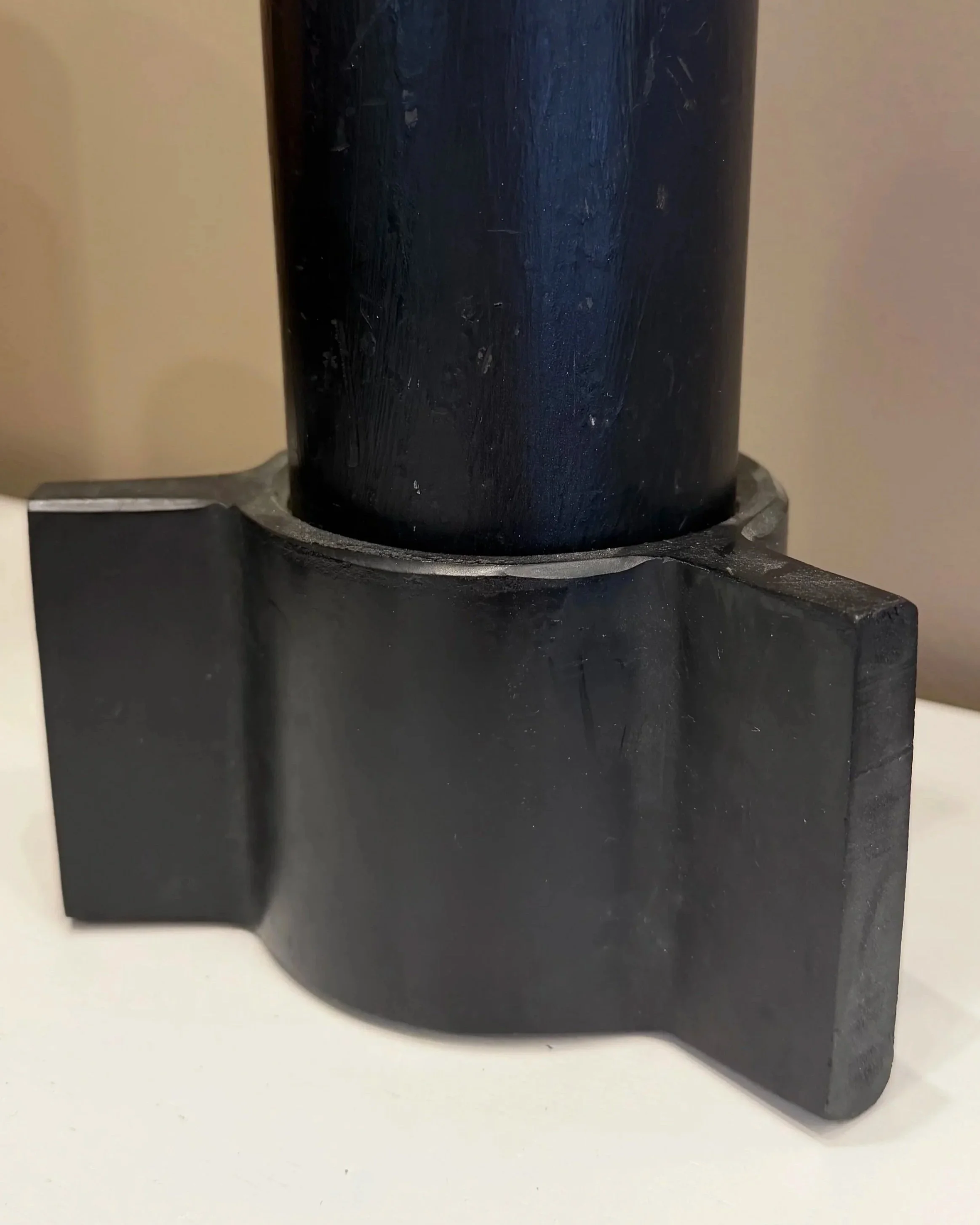 Close-up of a black cylindrical object, possibly a machine part or tool, with a textured surface, mounted on a black base, against a light-colored background.