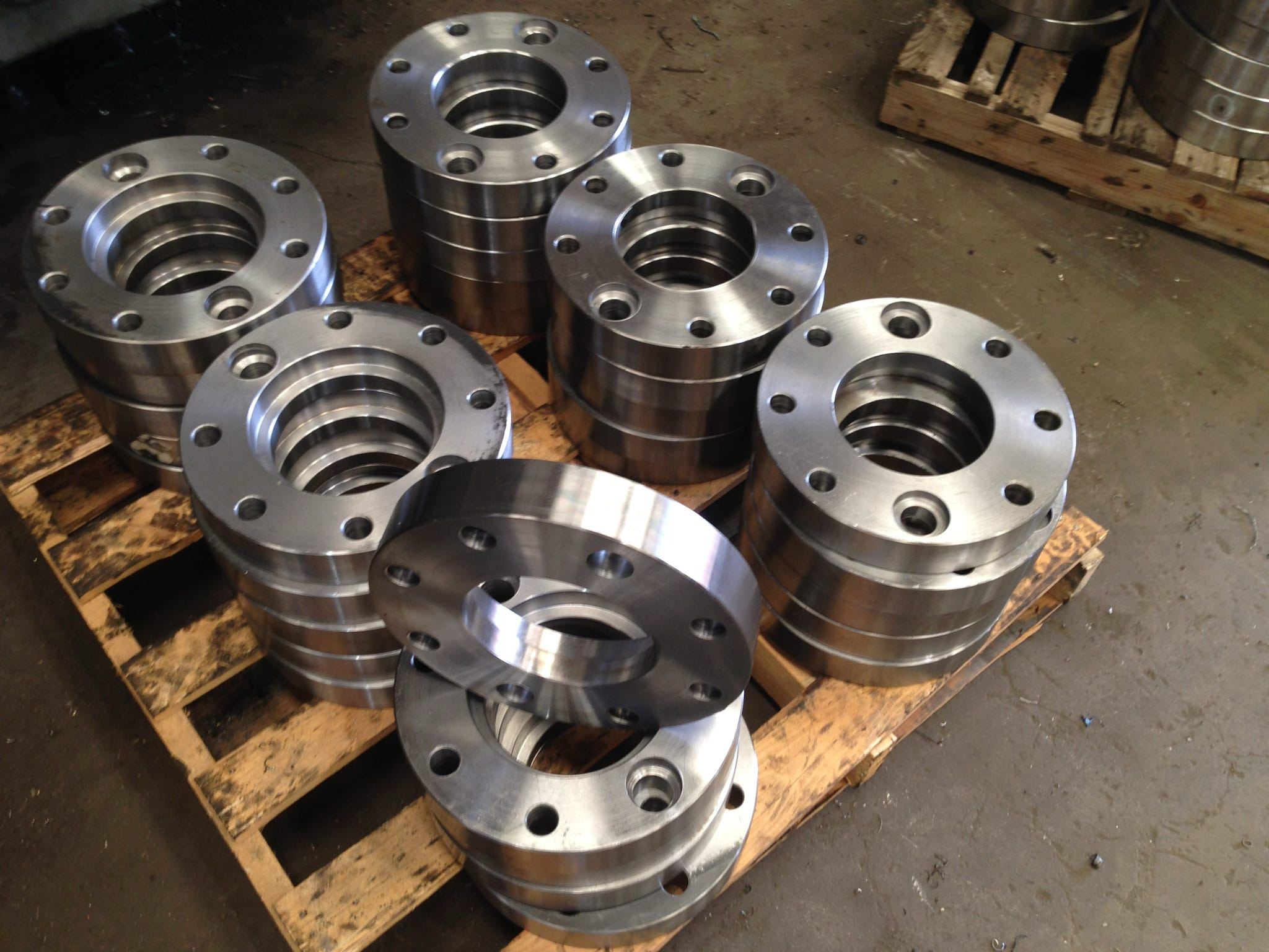 Multiple large metal machined rings stacked on wooden pallets in an industrial setting.