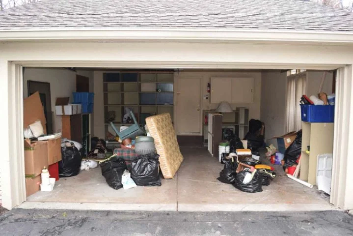 Garage filled with clutter, including boxes, bags, furniture, and miscellaneous household items.