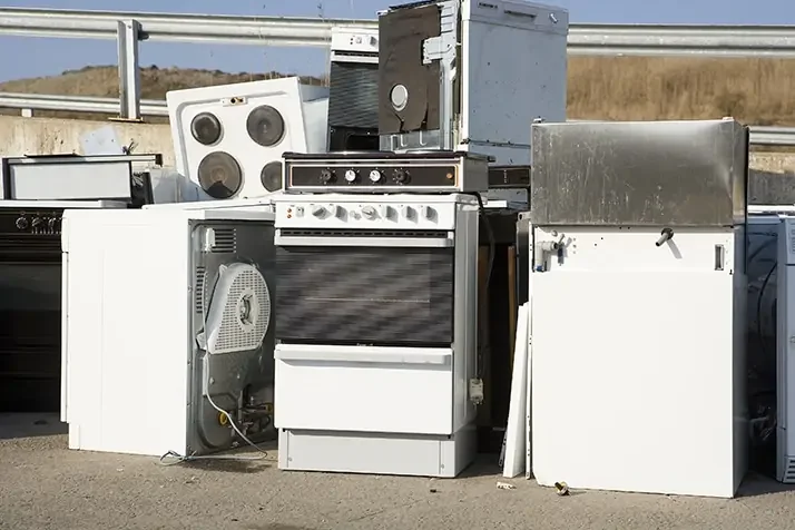 A pile of used appliances including stoves, ovens, and refrigerators.