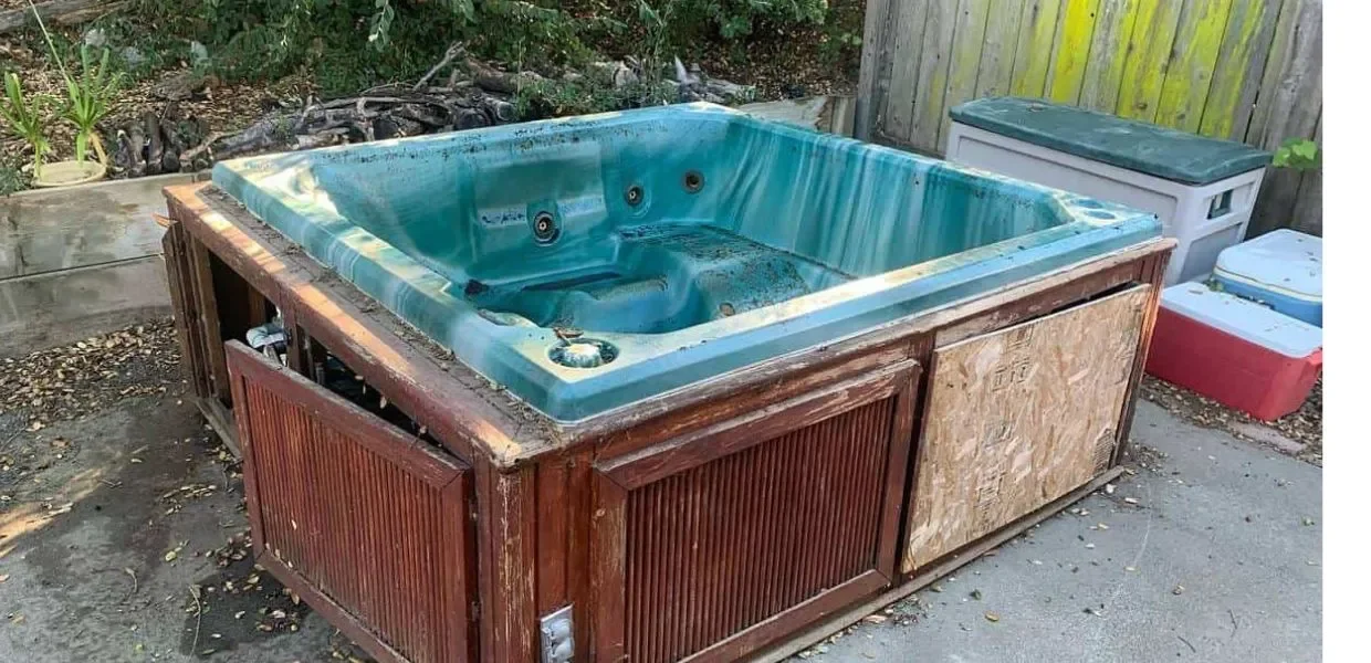 A hot tub with a wooden exterior being repaired outdoors, surrounded by debris and tools.