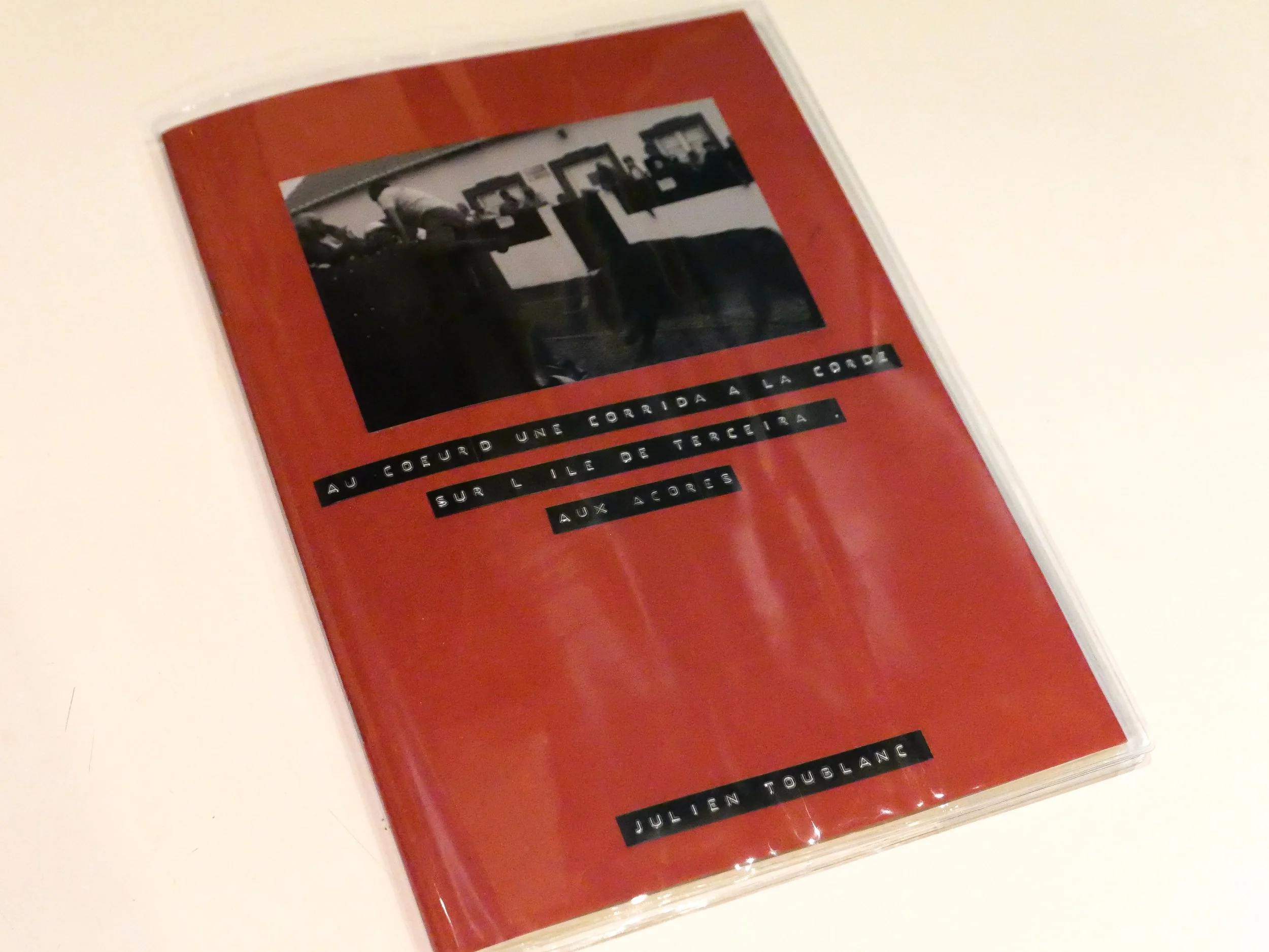 Livre photo artisanal avec une couverture rouge, titre en français réalisé avec une dymo, photographie en noir et blanc en haut, nom de l'auteur en bas du livre.