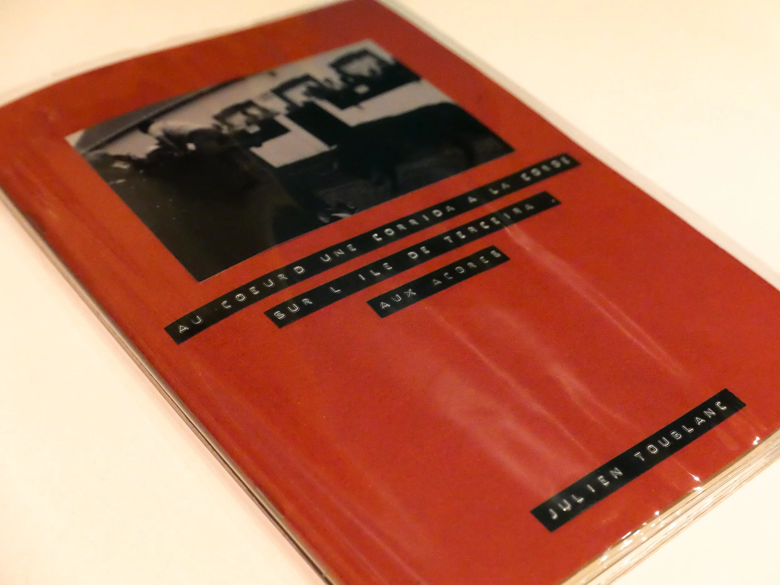 Couverture rouge d'un livre photo artisanal avec une photo en noir et blanc en haut, titre en français en noir et blanc, nom de l'auteur en bas : Julien Toublanc.