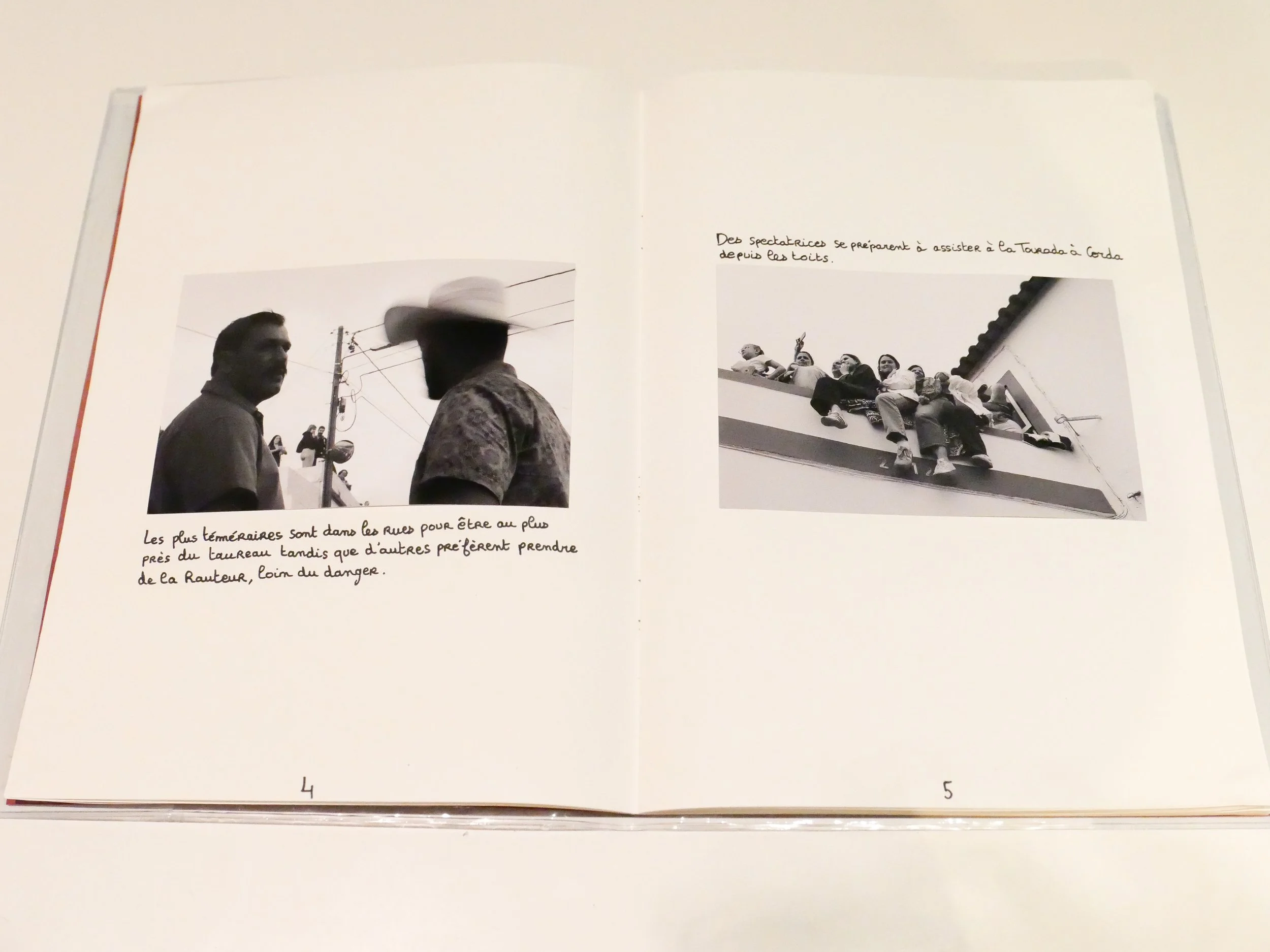 Deux pages d'un livre avec des photos en noir et blanc. La page de gauche montre deux hommes en conversation, l'un portant un chapeau. La page de droite montre un groupe de personnes assises sur un toit, regardant en bas.