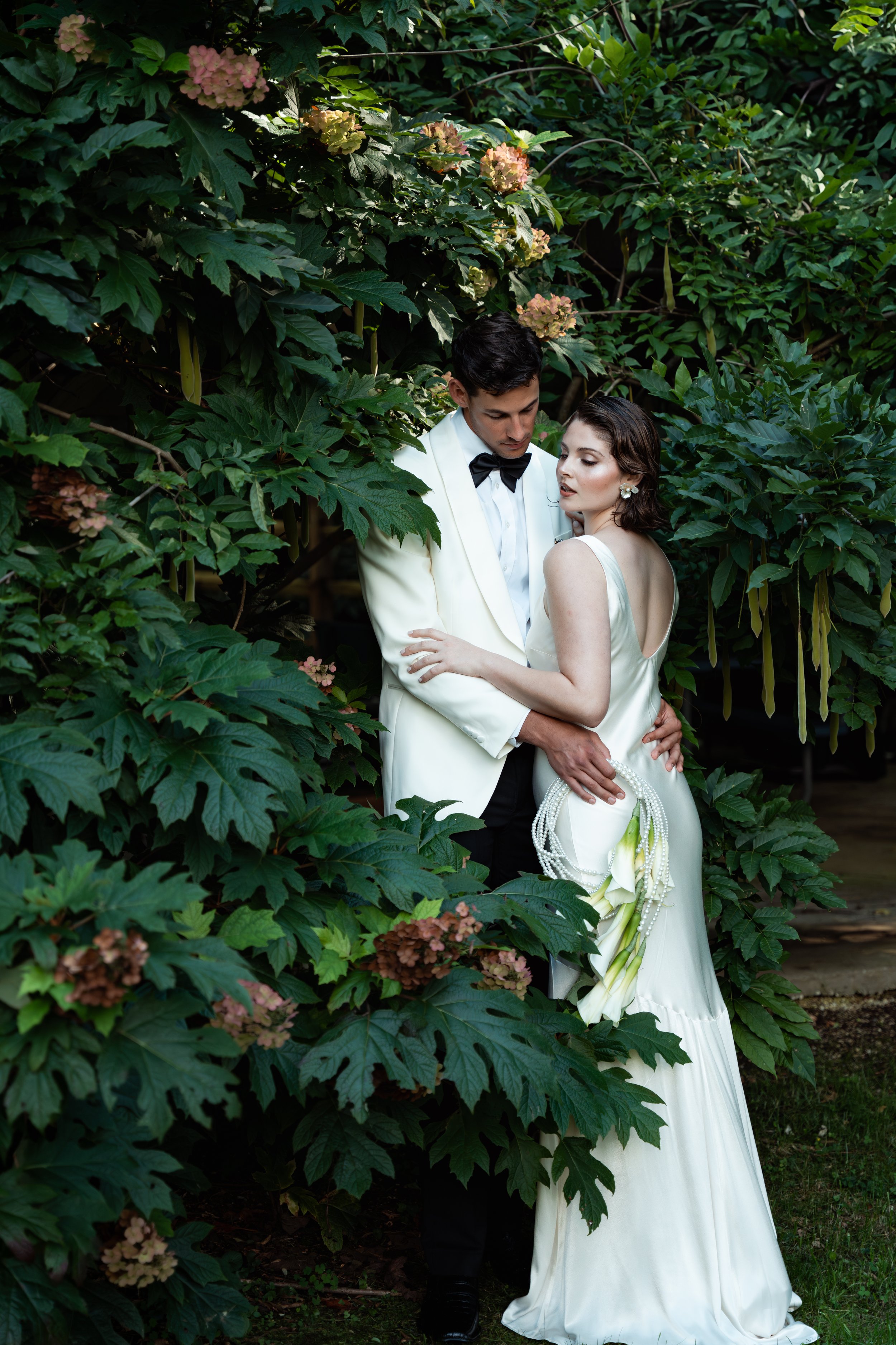 Couple beneath the vine-covered pavilion at Caya Azul, surrounded by flowers at an intimate mountain wedding near Asheville.