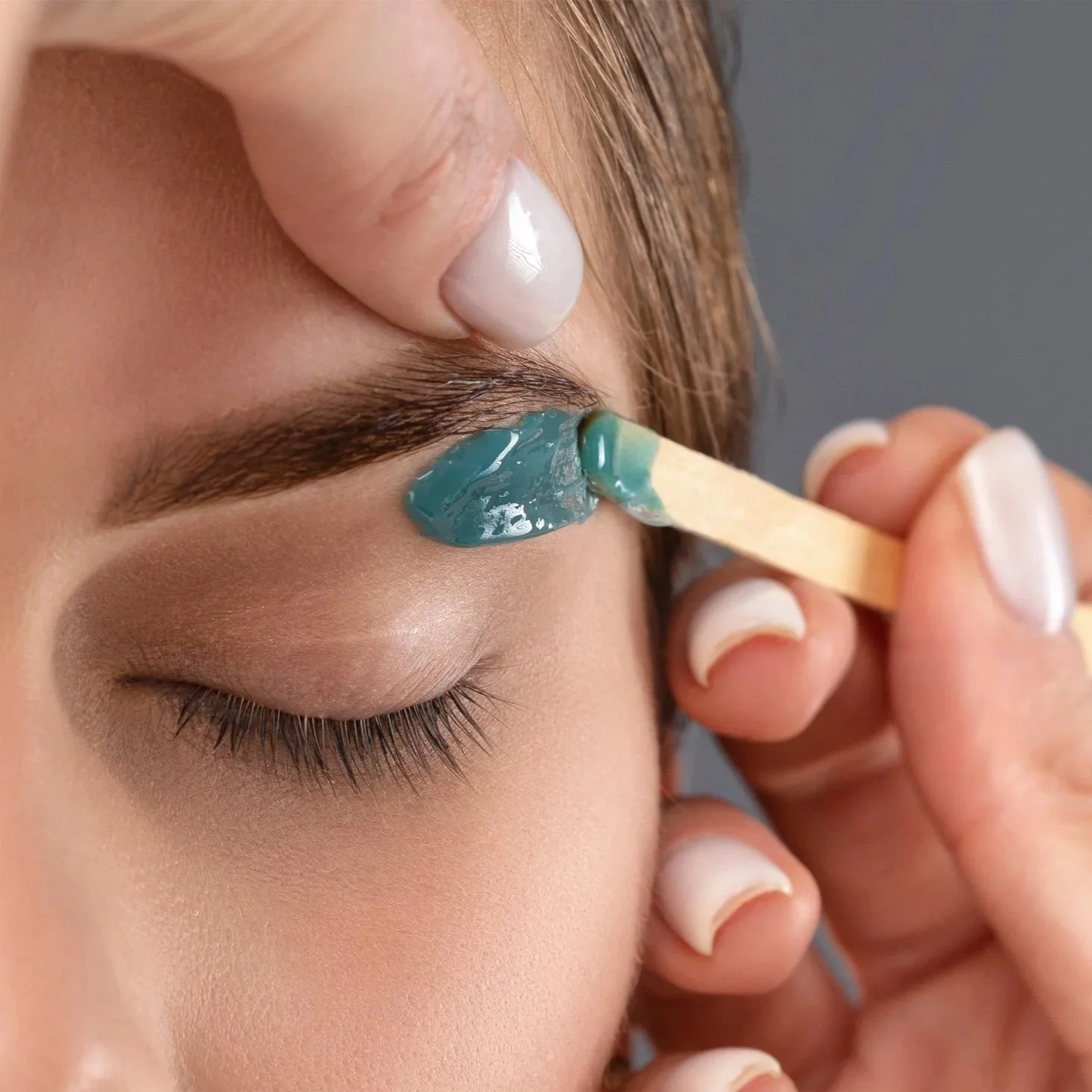 A person applying eyelash glue on their eyelid with a wooden spatula.