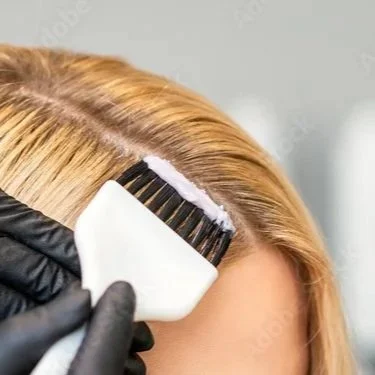 Close-up of a hairdresser applying dye to a person's blonde hair using a brush.