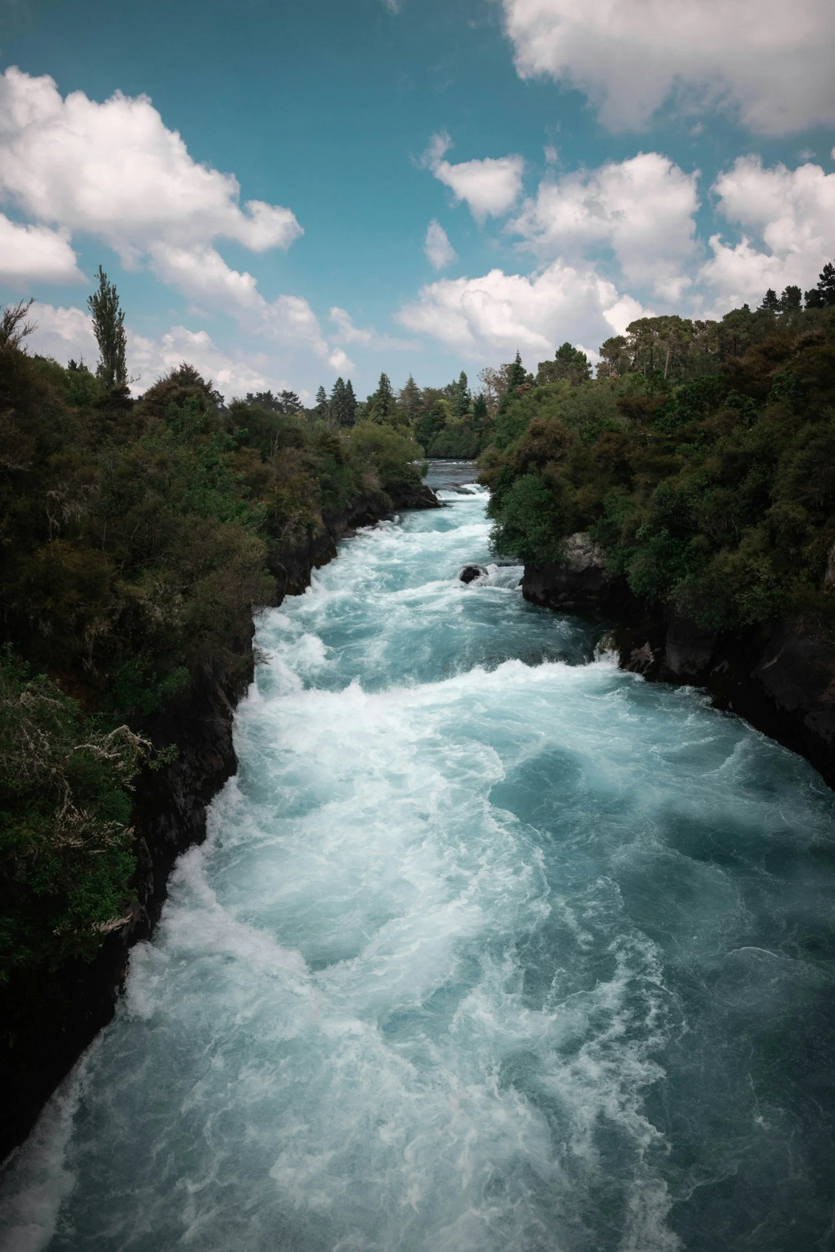 A river flowing rapidly between forested banks under a partly cloudy sky.