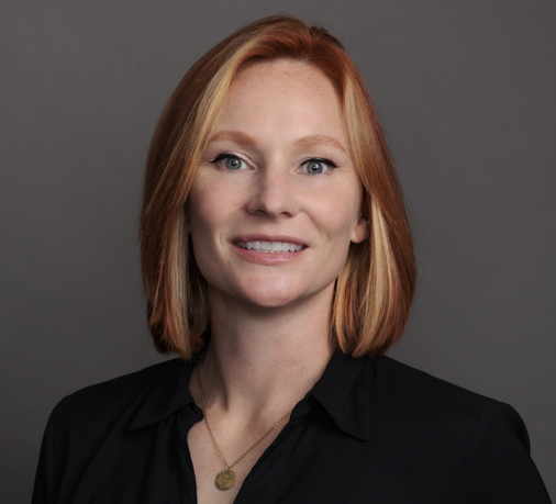 A woman with short hair, smiling, wearing a necklace and a black top, with a bright orange background.