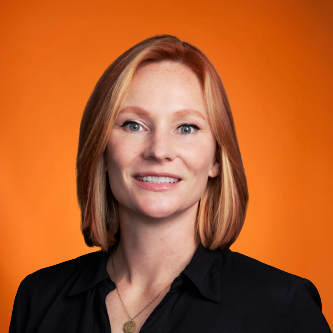 A woman with short hair, smiling, wearing a necklace and a black top, with a bright orange background.