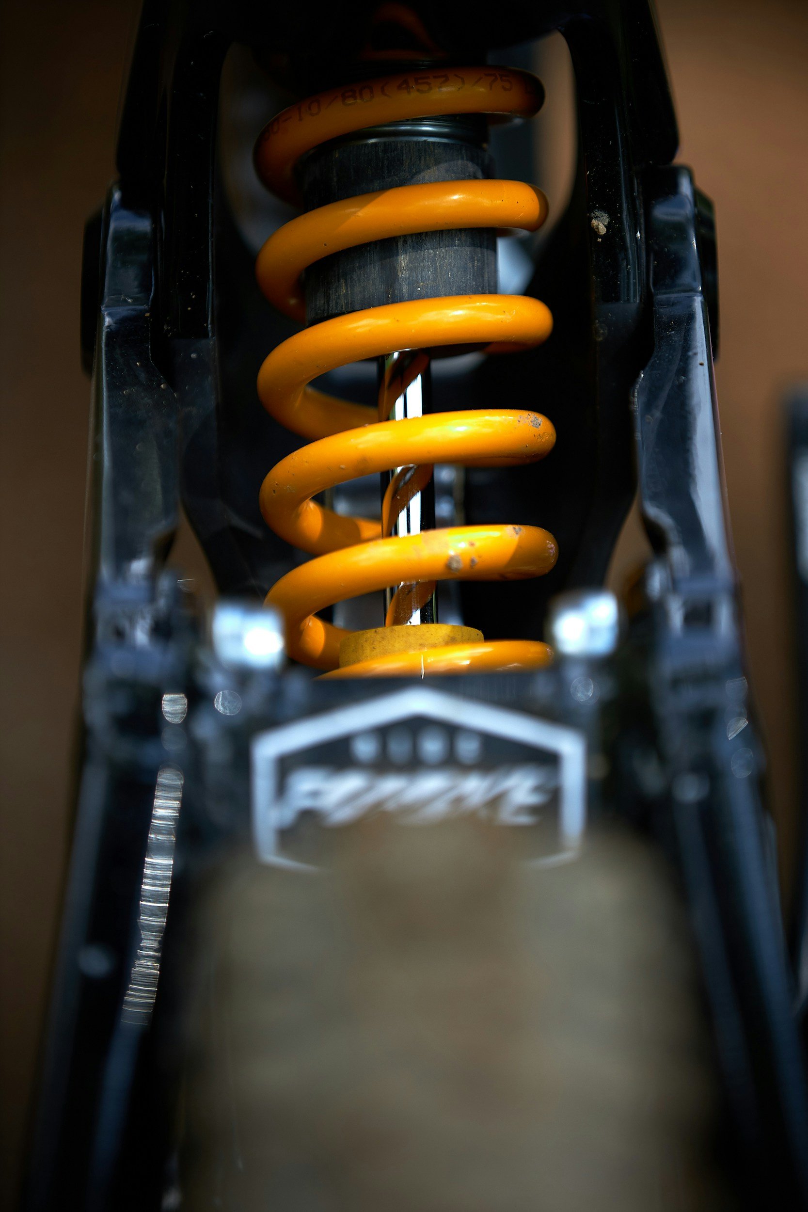Détail d'une suspension de vélo avec une fourchette et un ressort orange monté sur une structure noire. entretien 50 heures, 200 heures, shock, fourche, fox36, fox38, coid, rockshox