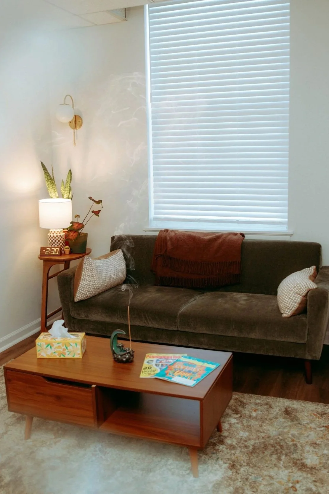 A cozy living room with a brown sofa, a wooden coffee table, a lamp, a tissue box, and magazines. Smoke is rising from a incense holder on the coffee table, and a clock on the side table shows 2:30.