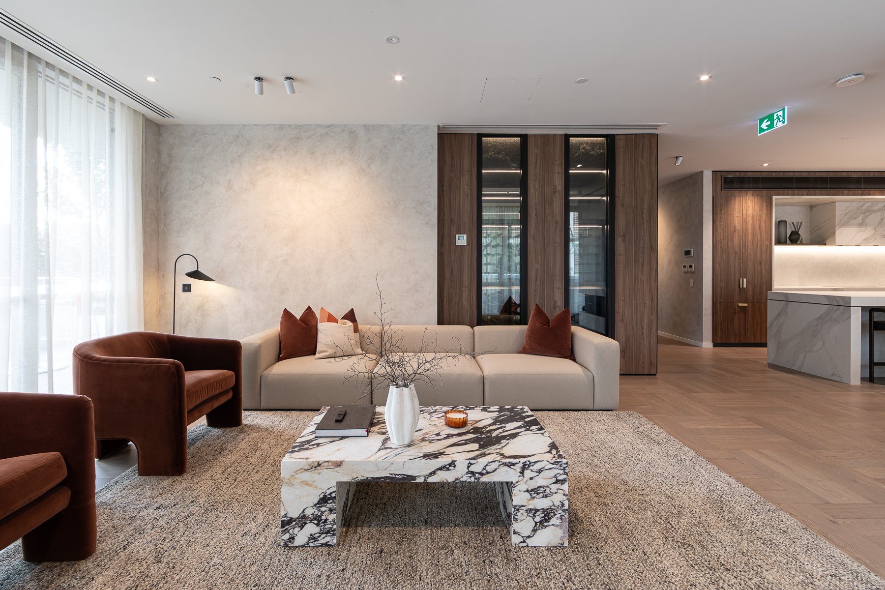 Modern living room with beige sofa, brown armchairs, marble coffee table, and minimalist decor.