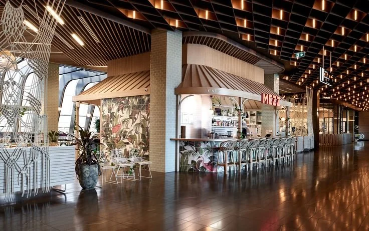 Interior of a modern restaurant or bar area with a tropical-themed backdrop, bar counter with stools, and decorative lighting.