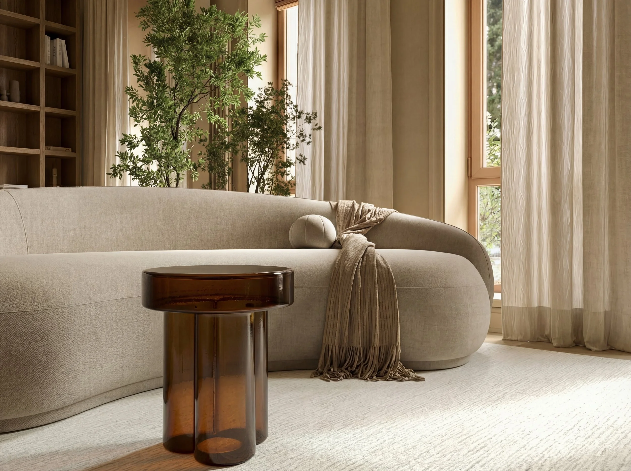 A cozy living room with a light beige sofa, a brown glass side table, and large windows with sheer curtains. There is a green potted plant behind the sofa, adding a touch of nature.