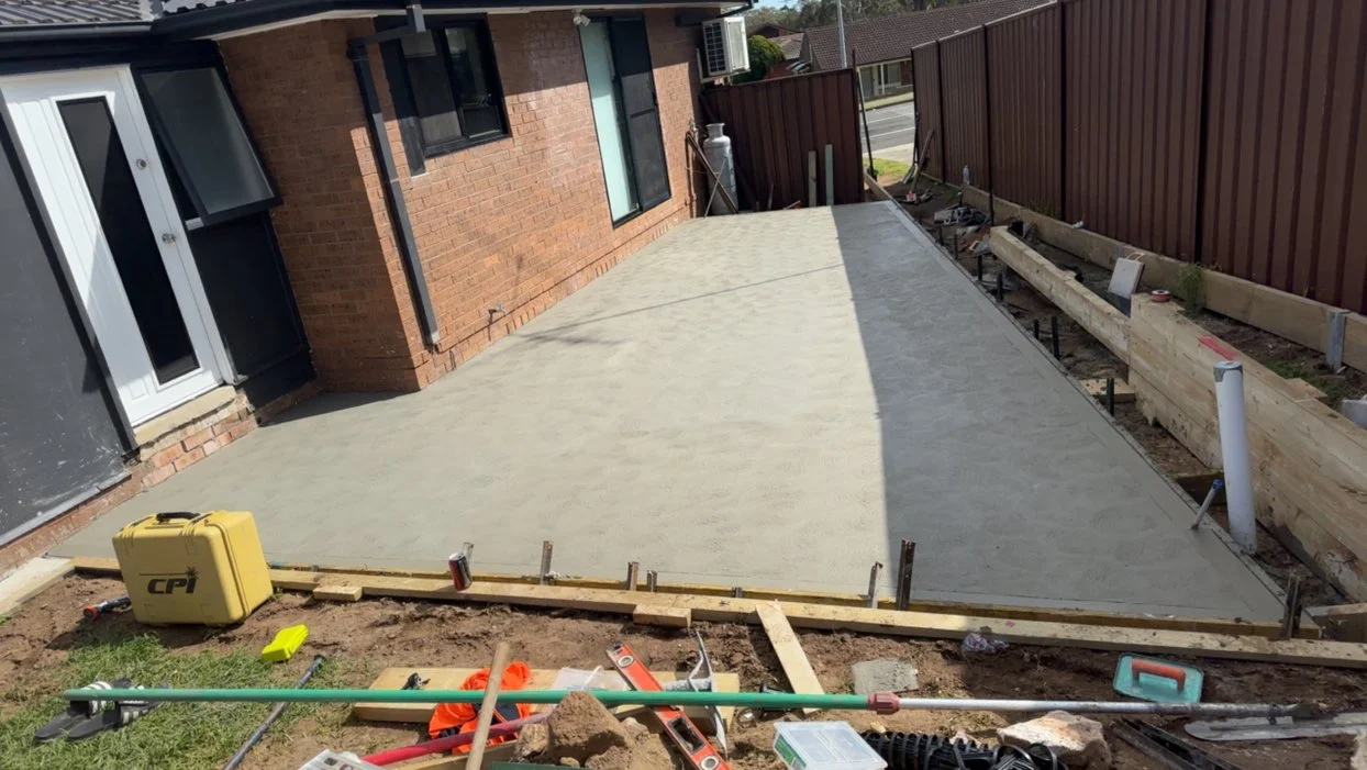 View of a freshly poured concrete patio next to a brick house,