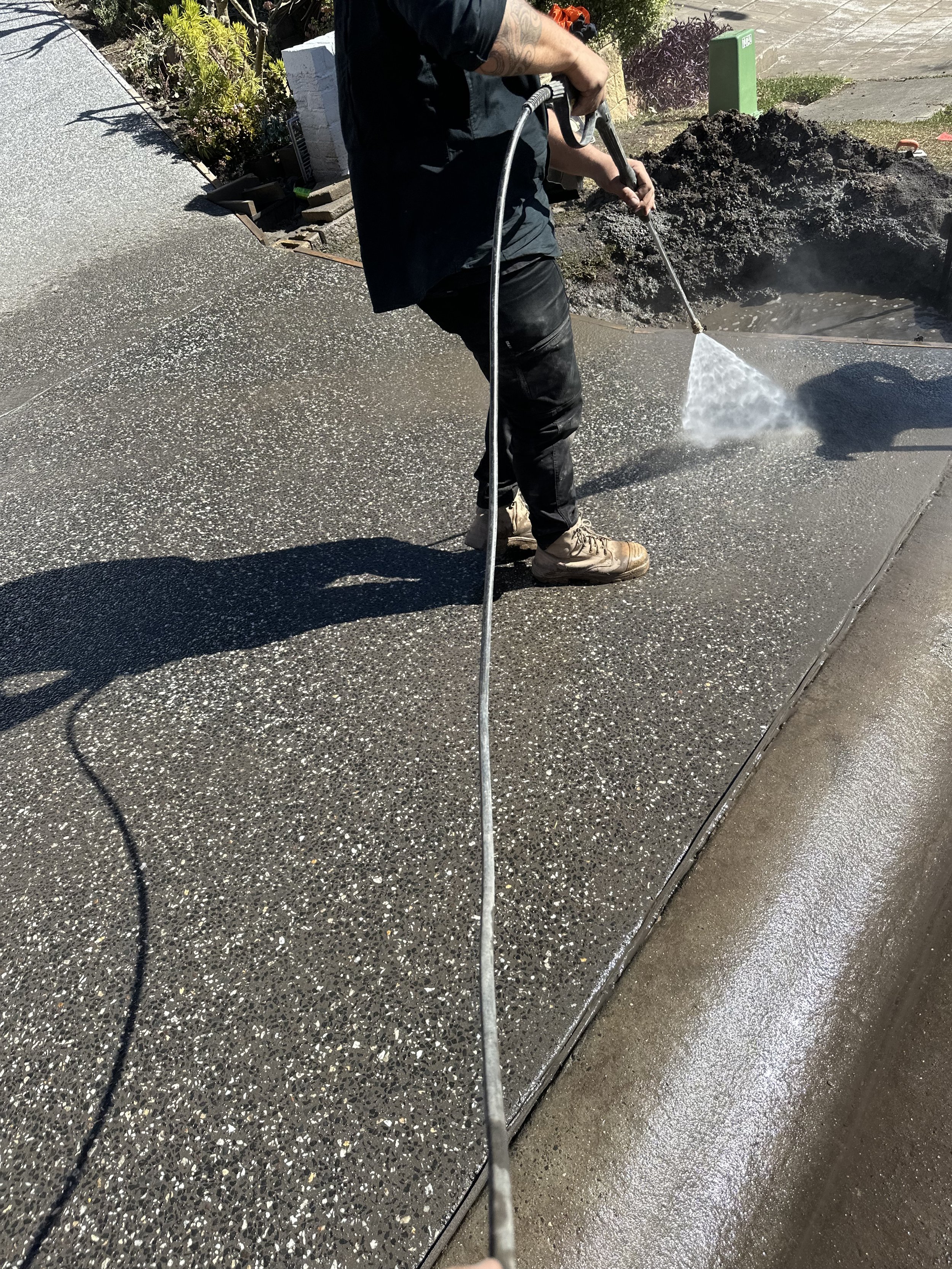 Worker spray cleaning a textured concrete sidewalk with a pressure washer.