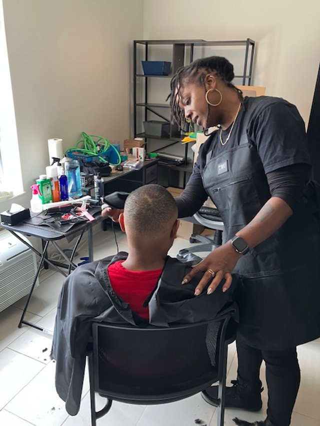 A woman getting a haircut from a hairstylist in a salon or barbershop.