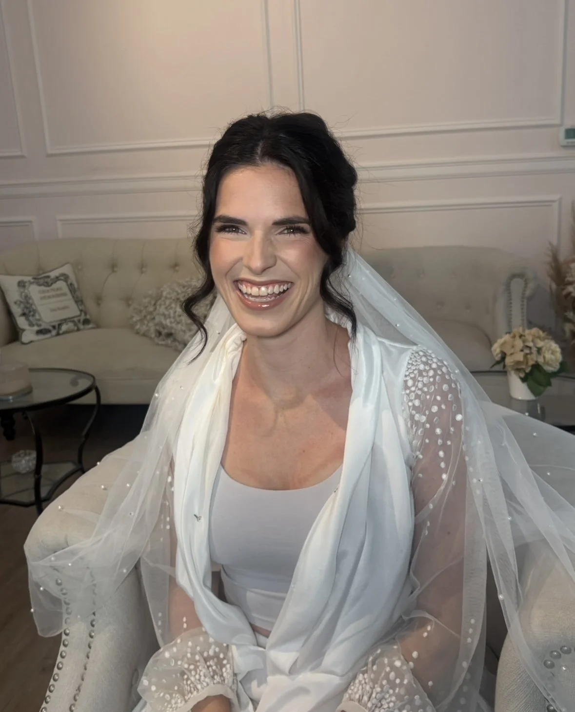 Smiling black haired bride with her hair in a bun wearing a white robe and flowing white veil