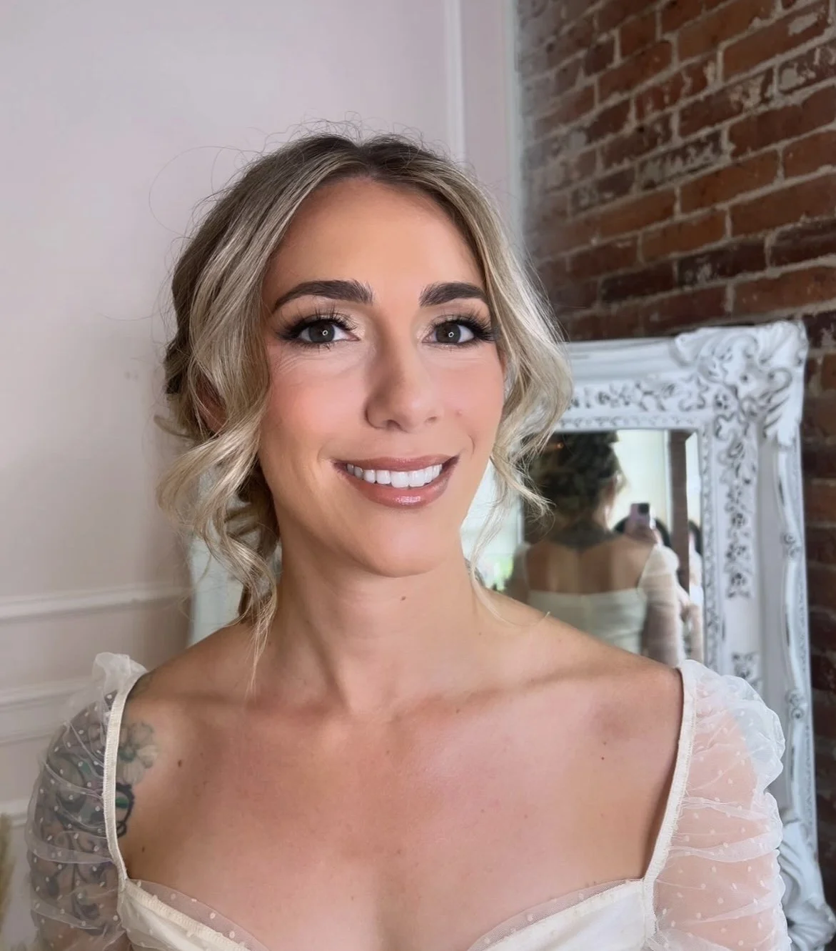 Bride with blonde hair in a low bun wearing a white top with see through sleeves