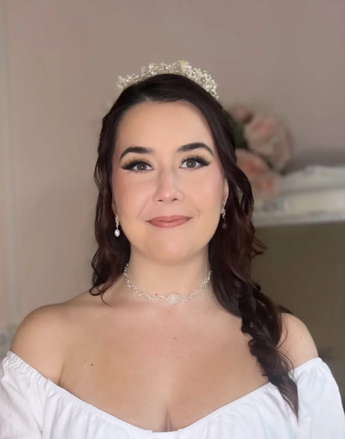 Brown haired bride wearing a white off the shoulder top with dangling earrings and a tiara