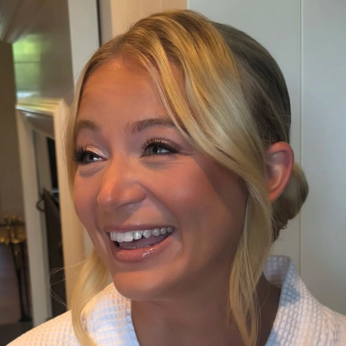 Blonde haired bride with a low bun, brown eyeliner, blue eyes, and a happy smile