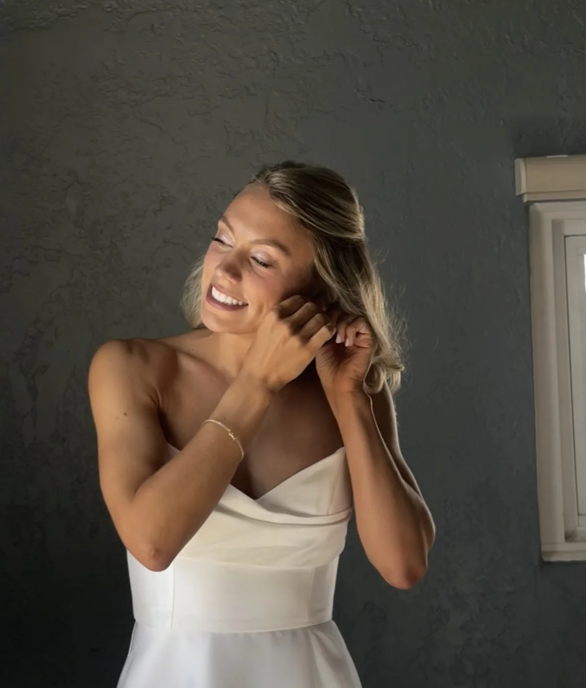 Blonde haired bride smiling while putting an earring in