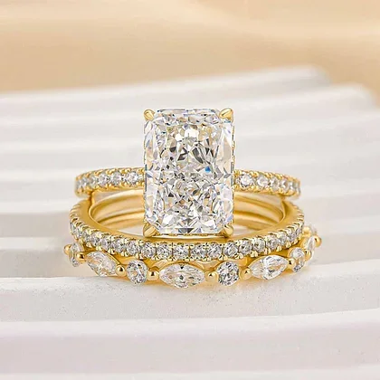 Close-up of a large rectangular diamond engagement ring with a gold band and smaller diamonds along the band, placed on a white surface.