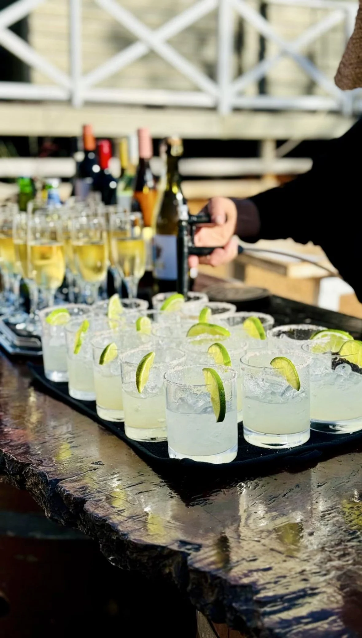 Tray of glass margaritas with lime garnishes on a wooden table at a wedding party.