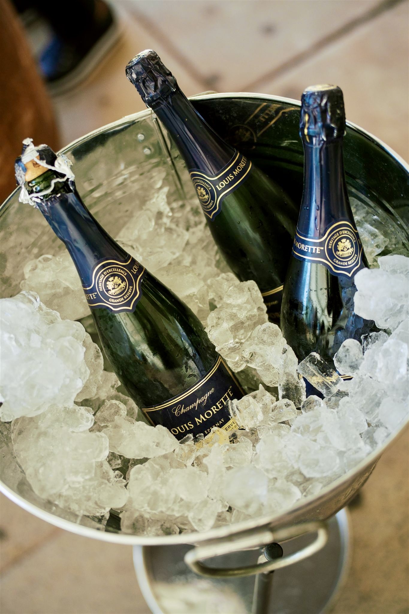 Three bottles of Louis Morette champagne chilling in a metal ice bucket filled with ice.