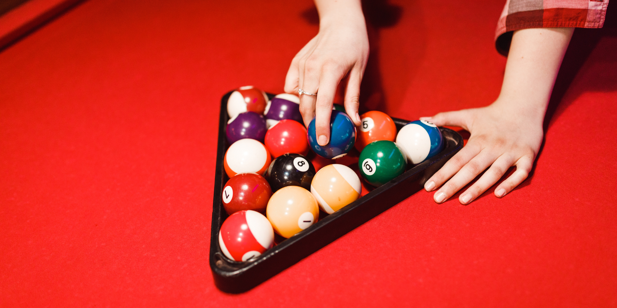 Person arranging billiard balls on a red pool table.