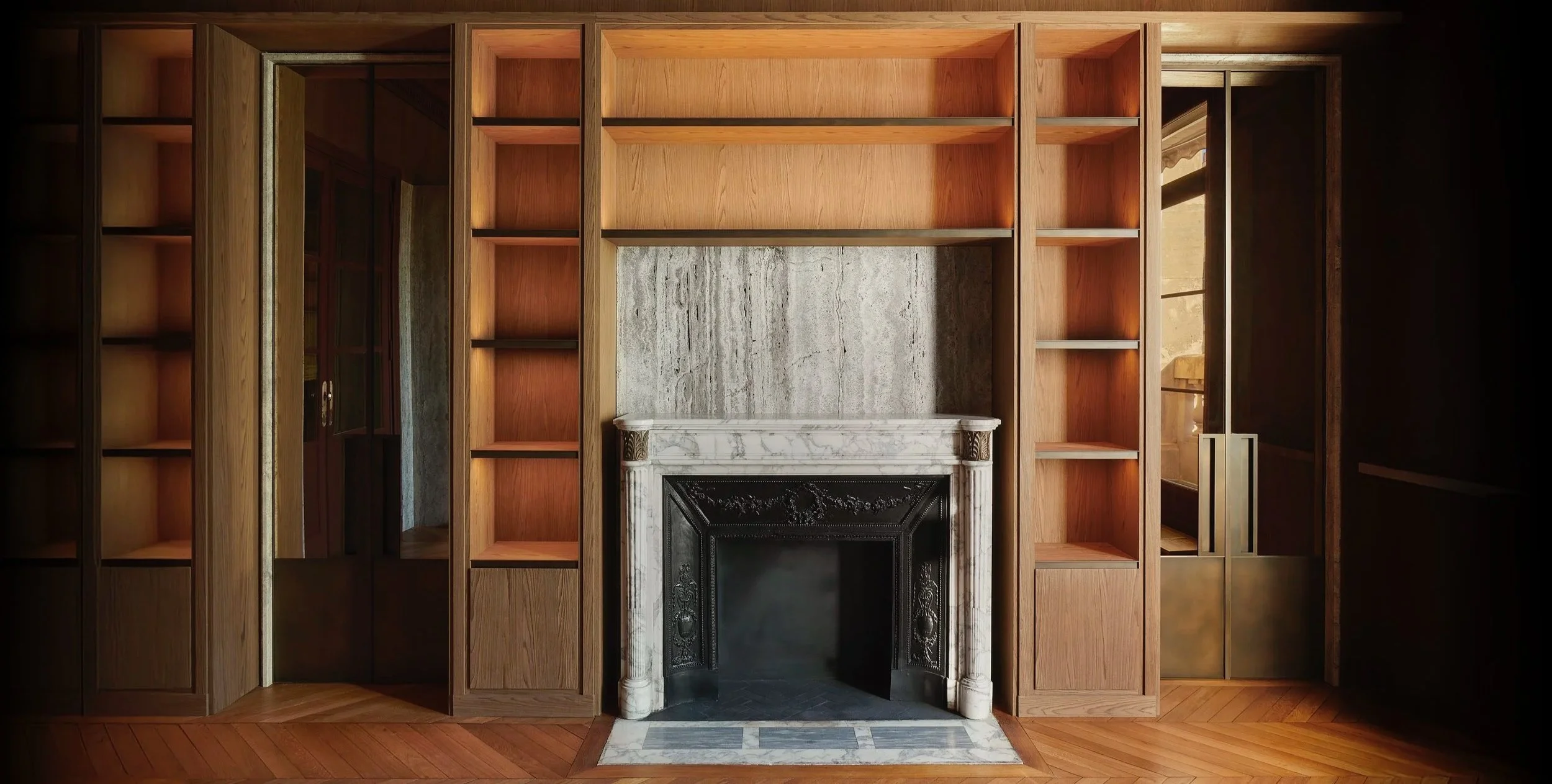 agencement d'une bibliothèque en chêne avec éclairage, cheminée d'époque en marbre, trumeau en travertin, portes en laiton patiné. fabrication et pose par Lamellux ébéniste agenceur